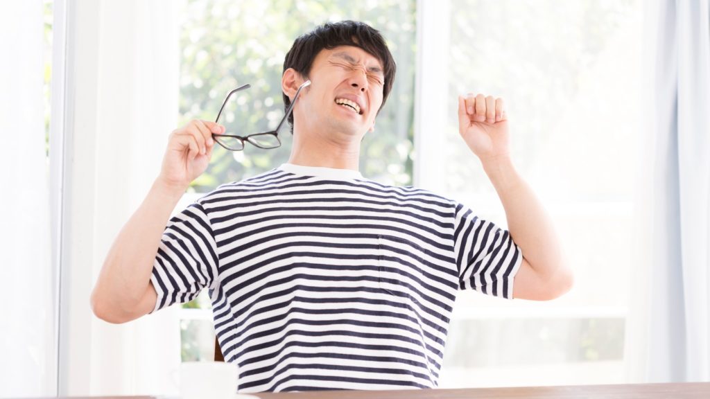 寝起きでも疲労感がとれず顔をしかめる男性の写真