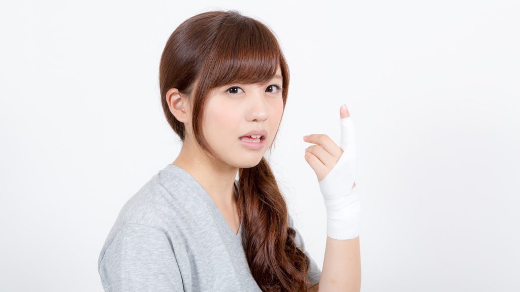 指の骨を折って治療された指先を見つめる女性の写真