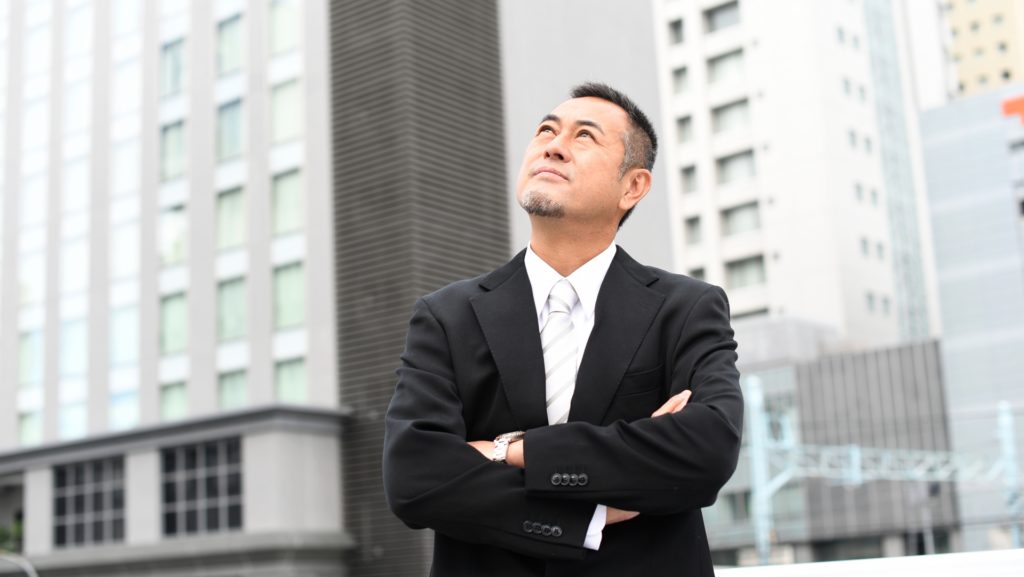 壮年の男性がビルの谷間から空を見上げている。ビジネスが上手くいくことを示唆している画像
