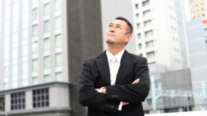 壮年の男性がビルの谷間から空を見上げている。ビジネスが上手くいくことを示唆している画像